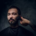 Portrait of pensive man with receive moustache and beard trimming procedure at barbershop.